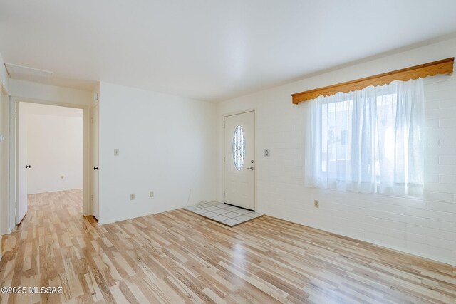 unfurnished dining area with beamed ceiling, brick wall, and light hardwood / wood-style flooring