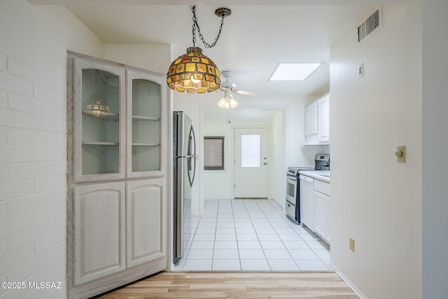 kitchen featuring visible vents, a skylight, ceiling fan, stainless steel appliances, and glass insert cabinets