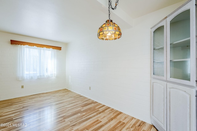 unfurnished room with light wood finished floors and brick wall