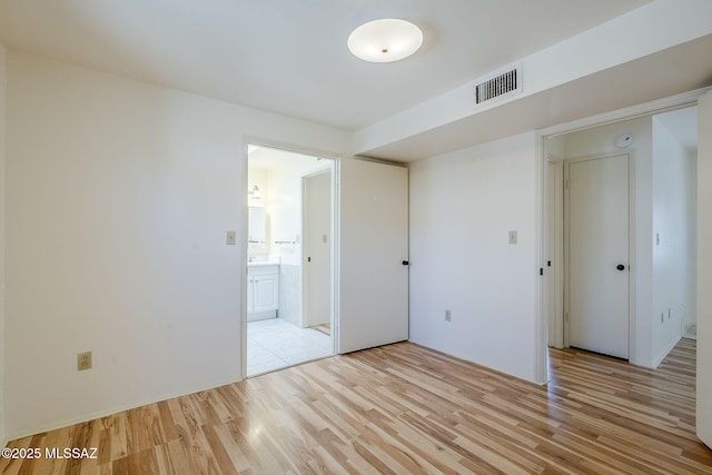 unfurnished bedroom with connected bathroom, visible vents, and light wood-type flooring