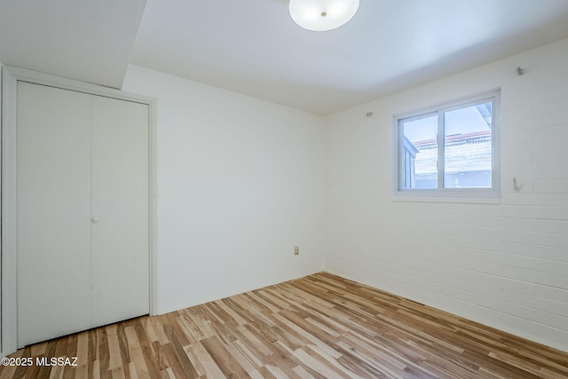 unfurnished bedroom featuring wood finished floors, a closet, and brick wall