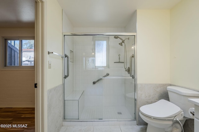 bathroom featuring a shower stall, toilet, tile walls, and wainscoting
