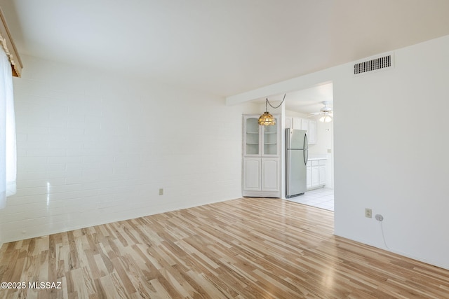 spare room featuring ceiling fan, visible vents, brick wall, and light wood-type flooring