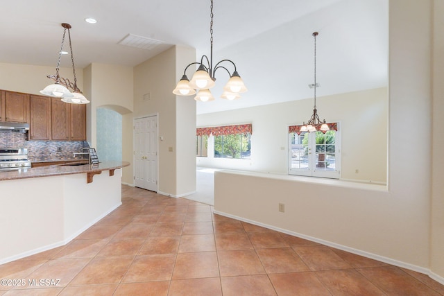 1474 N Miranda Ln, Green Valley, AZ 85614 - kitchen with brown cabinets, a chandelier, under cabinet range hood, stainless steel range with gas cooktop, and arched walkways