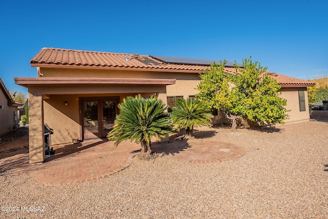 rear view of property featuring french doors and solar panels