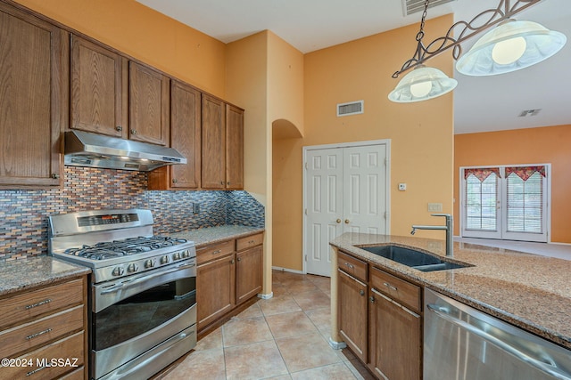 kitchen featuring light stone counters, sink, stainless steel appliances, and decorative light fixtures