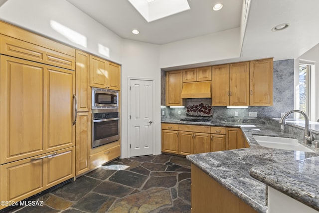 kitchen featuring premium range hood, sink, decorative backsplash, dark stone countertops, and appliances with stainless steel finishes