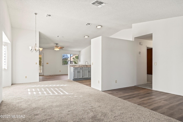 unfurnished living room featuring vaulted ceiling, sink, a textured ceiling, dark hardwood / wood-style flooring, and ceiling fan with notable chandelier