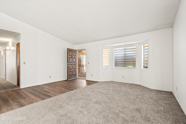 carpeted spare room featuring a textured ceiling and vaulted ceiling