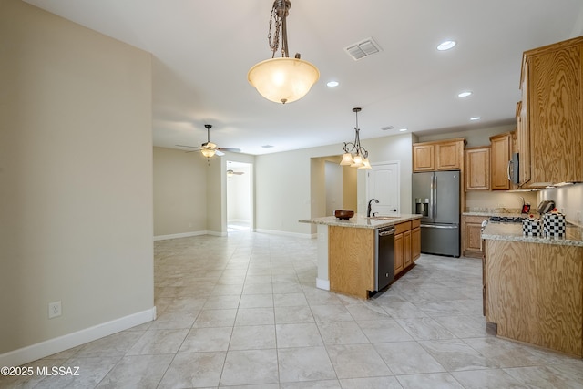 kitchen featuring decorative light fixtures, a kitchen island with sink, ceiling fan, light stone counters, and stainless steel appliances