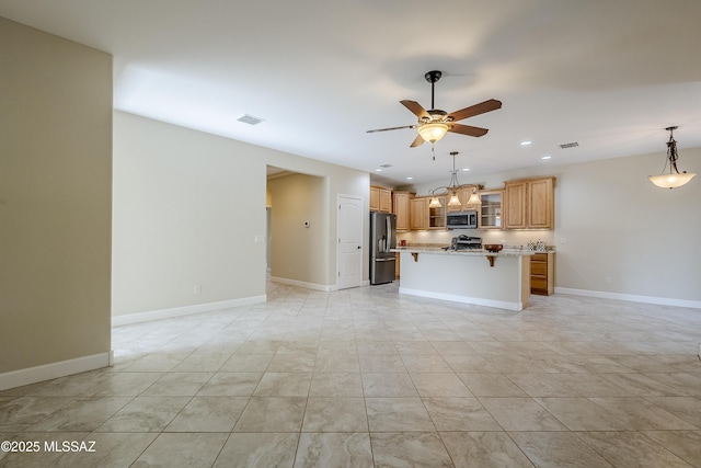 kitchen featuring ceiling fan, appliances with stainless steel finishes, a center island, light stone countertops, and a kitchen bar