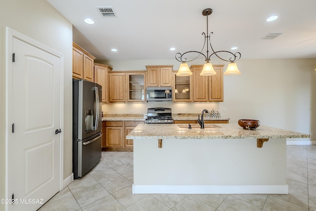 kitchen featuring sink, a breakfast bar area, appliances with stainless steel finishes, light stone countertops, and an island with sink