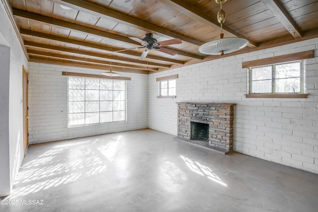 unfurnished living room featuring beam ceiling, a healthy amount of sunlight, and brick wall