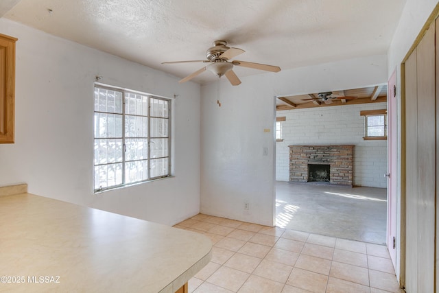 unfurnished living room featuring a stone fireplace, ceiling fan, light tile patterned floors, a textured ceiling, and brick wall