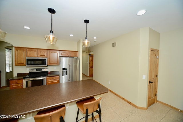 kitchen with appliances with stainless steel finishes, decorative light fixtures, light tile patterned floors, and a kitchen bar