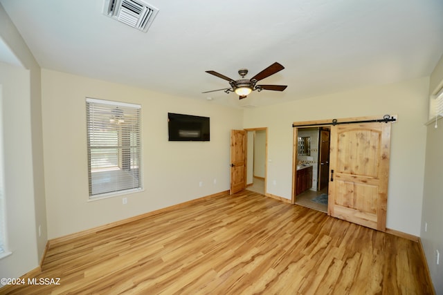 spare room featuring light wood-type flooring, ceiling fan, and a barn door