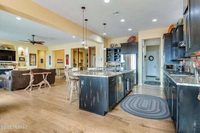 kitchen with light wood-style flooring, a large island, open floor plan, decorative light fixtures, and light stone countertops