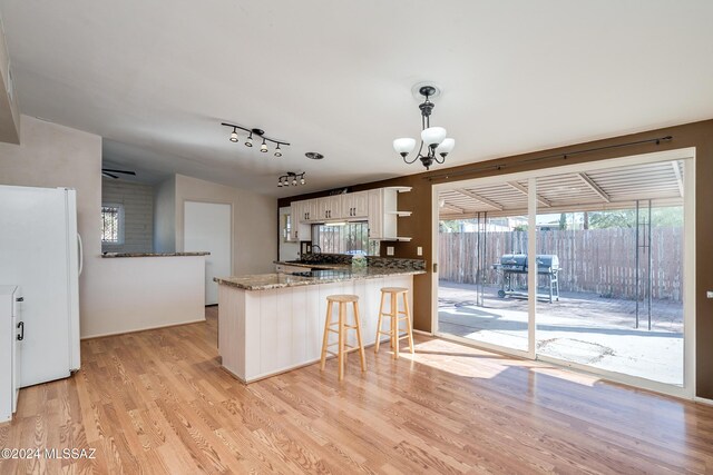 kitchen with kitchen peninsula, decorative light fixtures, light hardwood / wood-style flooring, white cabinets, and white fridge