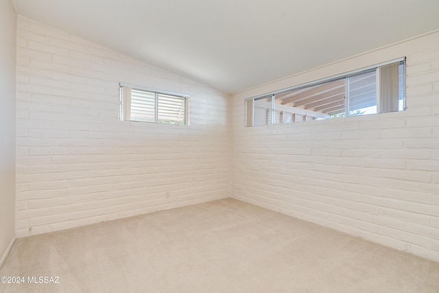 carpeted spare room featuring brick wall and vaulted ceiling