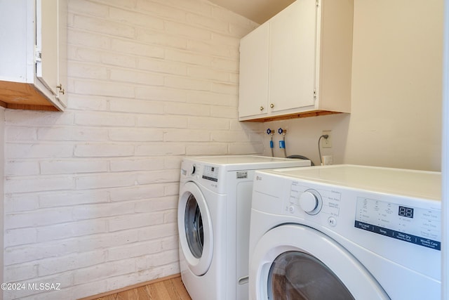 washroom with cabinets, light wood-type flooring, washer and clothes dryer, and brick wall