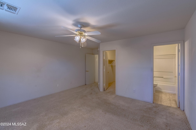 unfurnished bedroom featuring light carpet, a walk in closet, ensuite bathroom, ceiling fan, and a closet