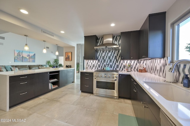 kitchen with high end stainless steel range, pendant lighting, wall chimney range hood, decorative backsplash, and sink