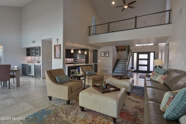 living room with ceiling fan with notable chandelier, a towering ceiling, beverage cooler, and bar area