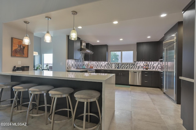 kitchen with wall chimney exhaust hood, a kitchen bar, stainless steel appliances, decorative backsplash, and kitchen peninsula