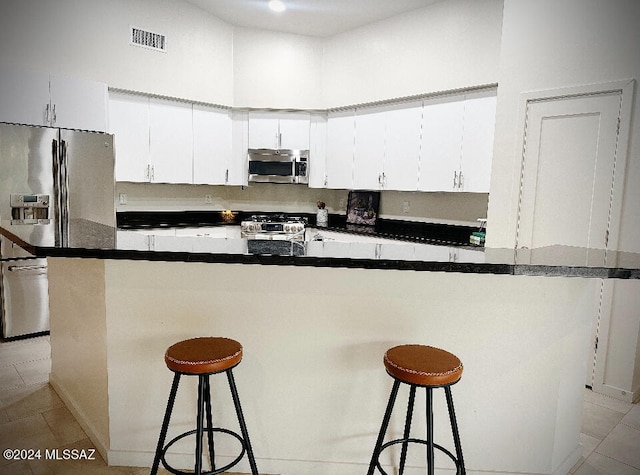 kitchen featuring light tile patterned floors, a kitchen bar, white cabinetry, and appliances with stainless steel finishes