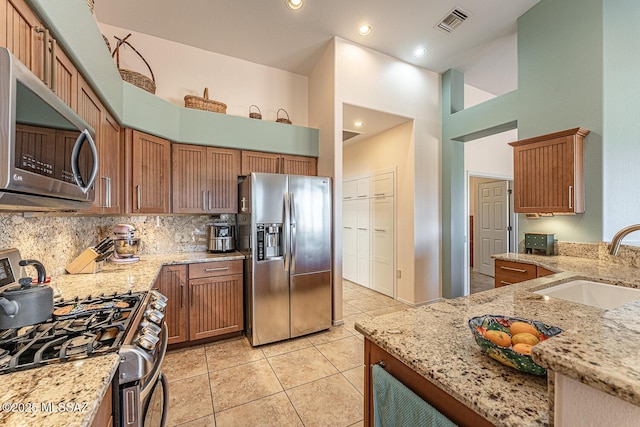 kitchen featuring sink, light tile patterned floors, appliances with stainless steel finishes, light stone countertops, and a high ceiling