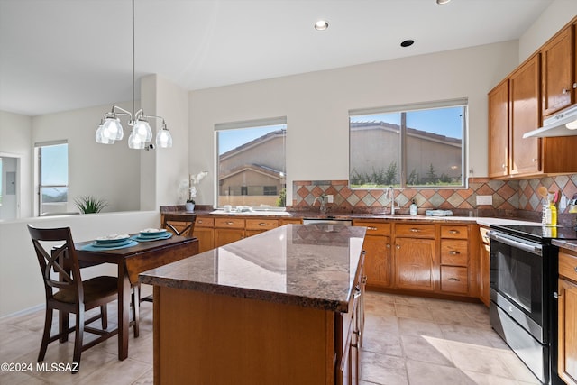 kitchen featuring backsplash, under cabinet range hood, dark stone countertops, stainless steel range with electric stovetop, and brown cabinets