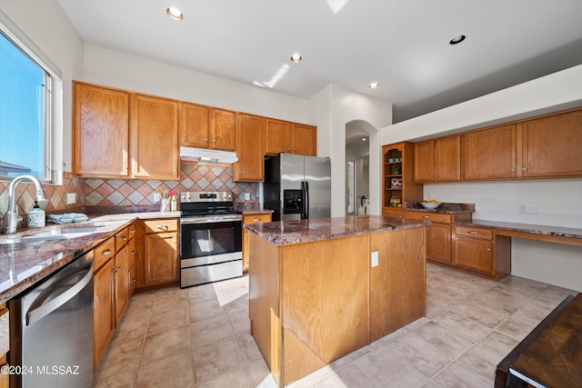 kitchen with a sink, under cabinet range hood, a center island, stainless steel appliances, and dark stone counters