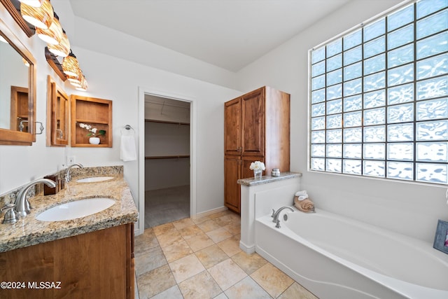 bathroom featuring a walk in closet, a garden tub, double vanity, and a sink