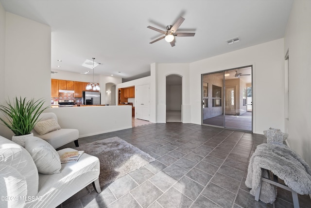 living area with stone finish floor, ceiling fan with notable chandelier, visible vents, and arched walkways