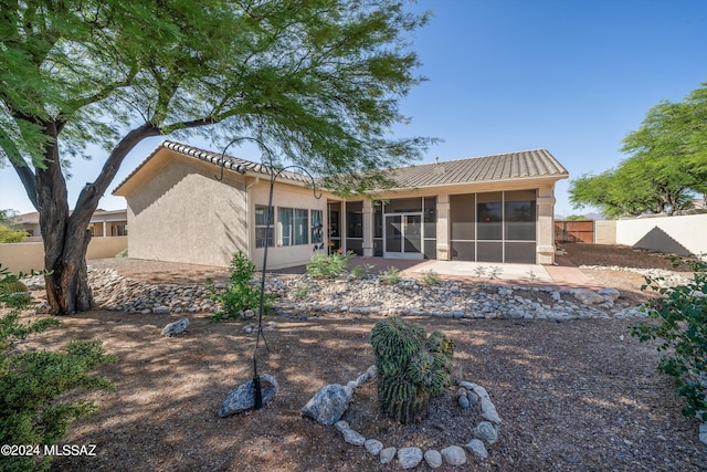 rear view of house with a tiled roof, stucco siding, a sunroom, and fence