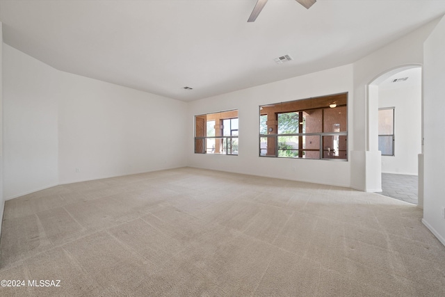 unfurnished room with arched walkways, visible vents, light colored carpet, and a ceiling fan