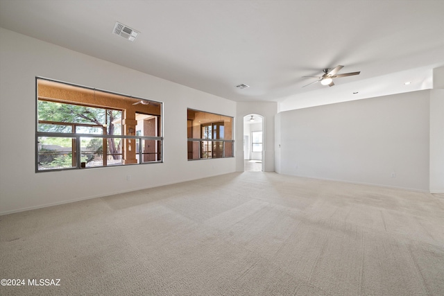 unfurnished room featuring light carpet, visible vents, arched walkways, and a ceiling fan