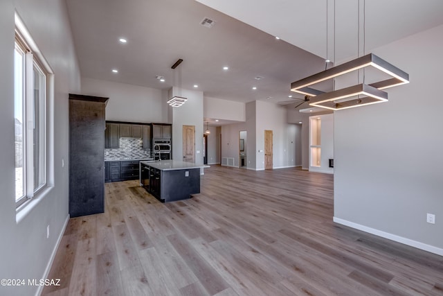 kitchen featuring a kitchen bar, decorative backsplash, hanging light fixtures, a kitchen island with sink, and light hardwood / wood-style floors