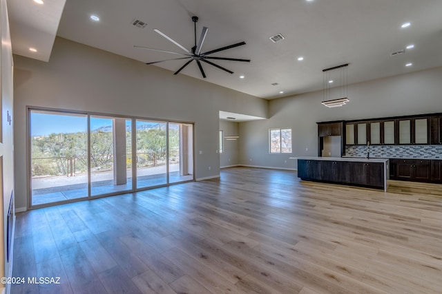 unfurnished living room featuring ceiling fan, a towering ceiling, sink, and light wood-type flooring