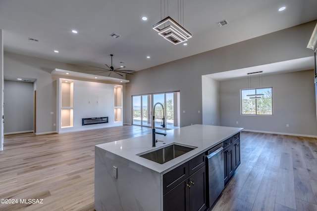 kitchen featuring an island with sink, dishwasher, sink, hanging light fixtures, and light wood-type flooring