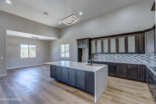 kitchen featuring pendant lighting, sink, light hardwood / wood-style flooring, a kitchen island with sink, and backsplash