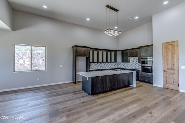 kitchen with pendant lighting, dark brown cabinets, an island with sink, and a high ceiling