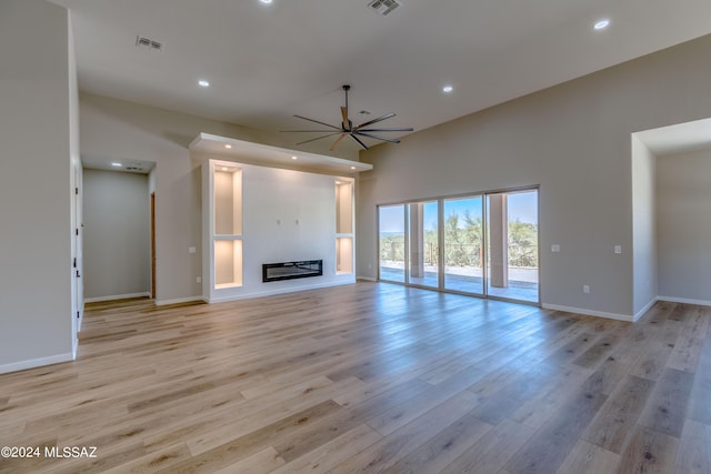 unfurnished living room with a towering ceiling, light hardwood / wood-style floors, and ceiling fan