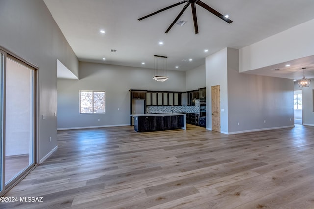 unfurnished living room with a high ceiling, ceiling fan with notable chandelier, and light hardwood / wood-style floors