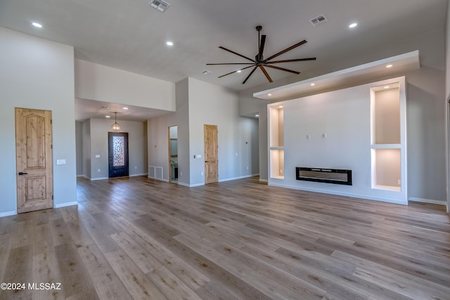 unfurnished living room featuring ceiling fan, light hardwood / wood-style flooring, and a high ceiling