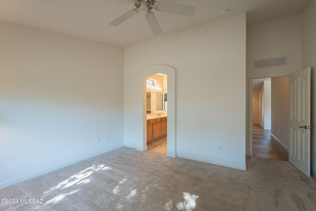 unfurnished bedroom with ceiling fan, ensuite bathroom, a towering ceiling, and light carpet