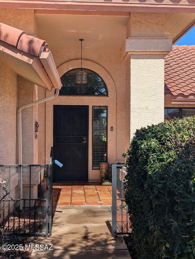 property entrance featuring a tiled roof, central AC unit, a gate, and stucco siding