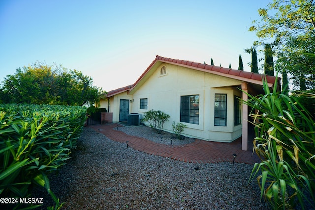 view of property exterior featuring central air condition unit, a patio area, a tiled roof, and stucco siding