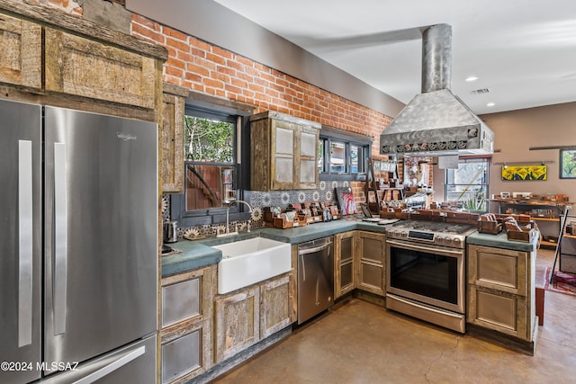 kitchen featuring island exhaust hood, appliances with stainless steel finishes, a healthy amount of sunlight, and brick wall