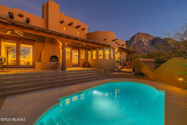 pool at dusk with a mountain view, french doors, and ceiling fan